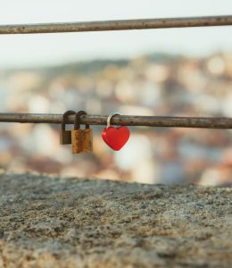 Close-up of padlocks, including a heart-shaped one, on a metal railing focused on a blurred urban background.